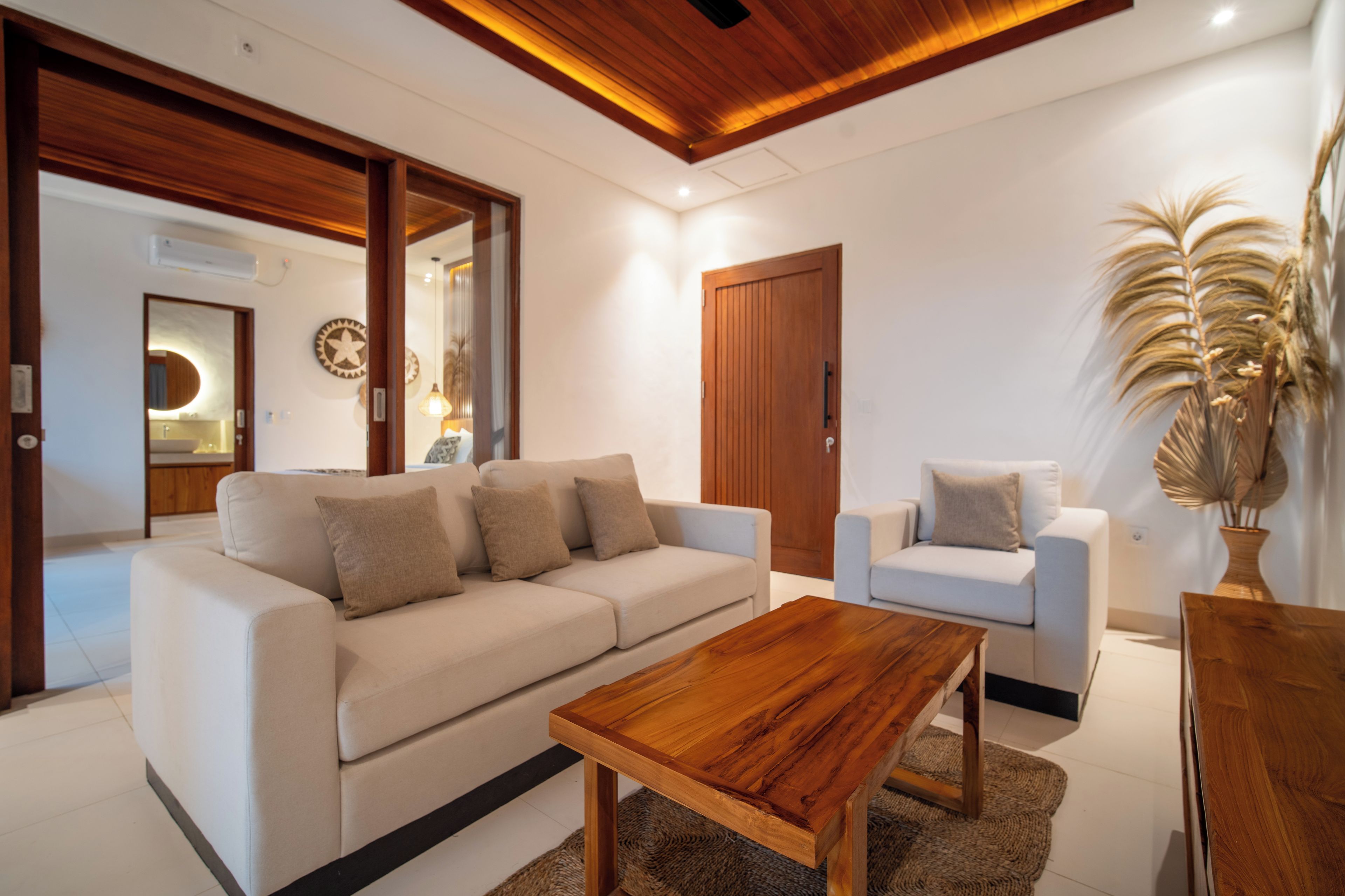 Una sala de estar moderna con un sofá color beige, una mesa de centro de madera y un sillón blanco.