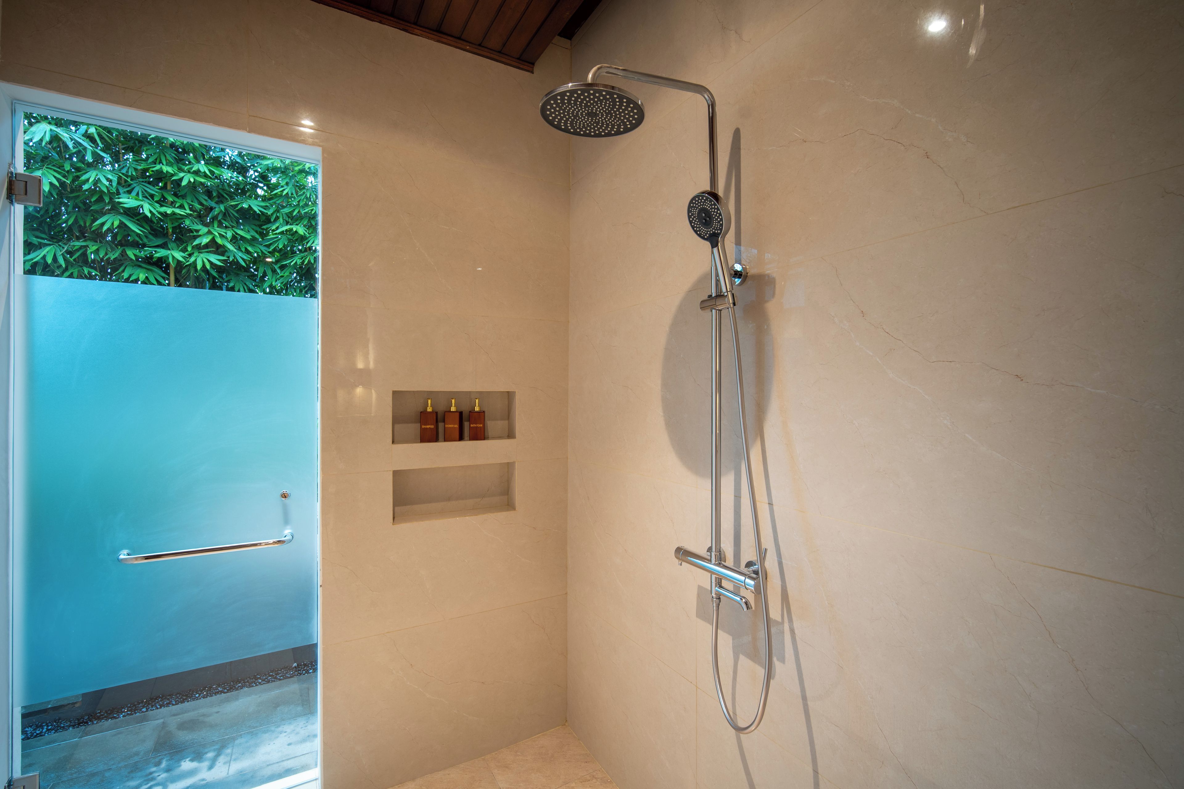 Un baño moderno con puerta de vidrio, ducha con cabezal de mano y estante con artículos de aseo.