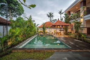 A swimming pool surrounded by lush greenery and a building with a tiled roof. - Yoga Sri Ubud (Gianyar)