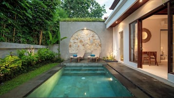 A swimming pool with two lounge chairs and a stone wall with a circular design.