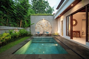 Una piscina con dos sillas reclinables y un muro de piedra con un diseño circular.