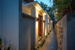 Un sendero estrecho que conduce a un edificio con una puerta de madera y una pared de piedra a un lado.
