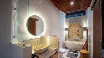 Un baño moderno con un lavamanos ovalado grande, una bañera independiente y un arco de pared de piedra.
