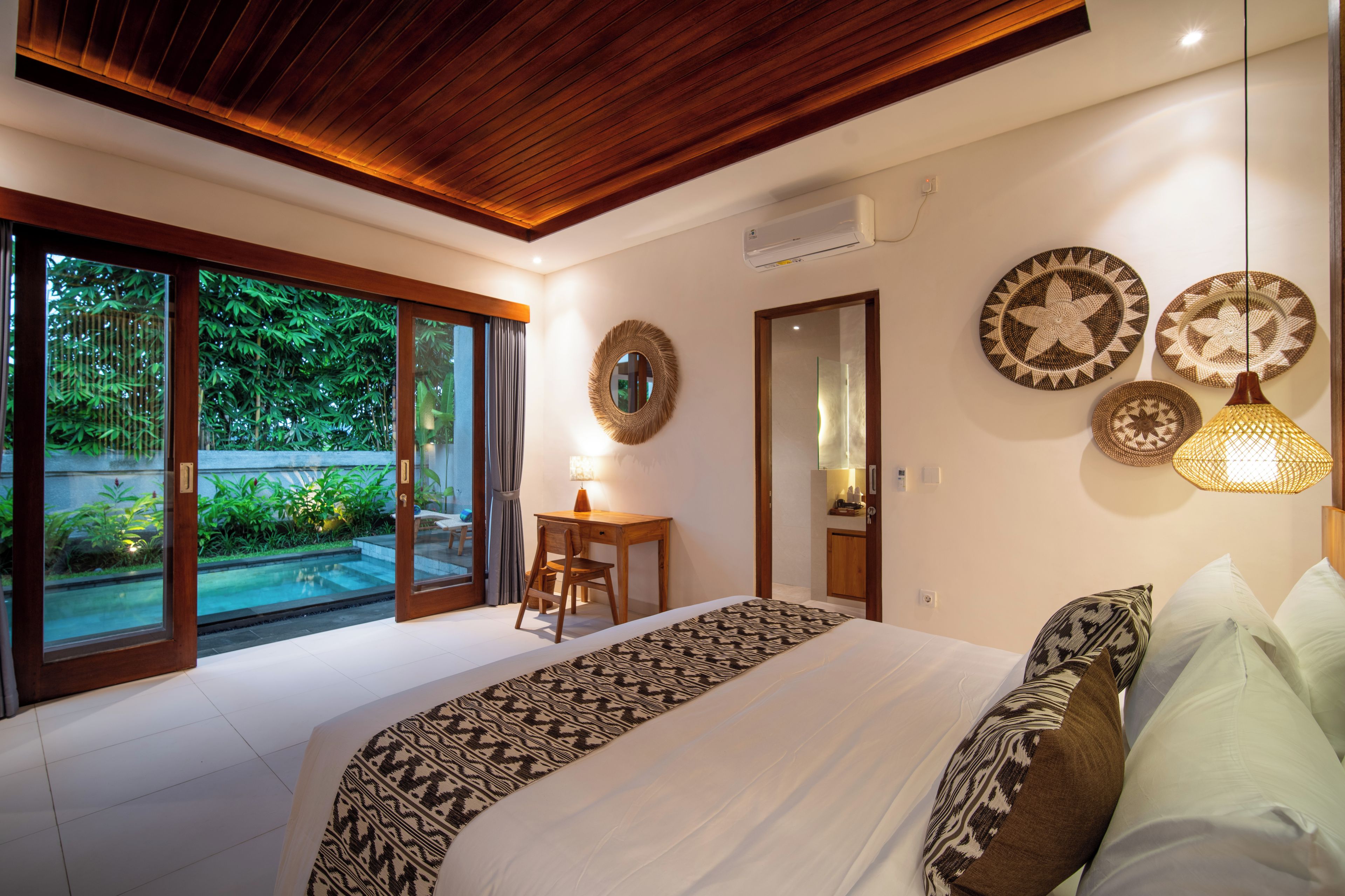 Un dormitorio con una cama grande, un escritorio y vistas a un jardín a través de puertas de vidrio.