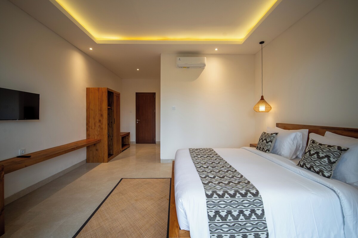 Un dormitorio moderno con una cama grande, un televisor montado en la pared, un banco de madera y una lámpara en el techo.