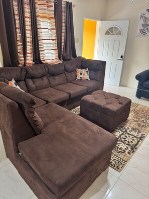A brown sectional sofa with a matching ottoman, a patterned rug, and a door with a window in the background. - THE ROSE GARDEN (Mandeville)