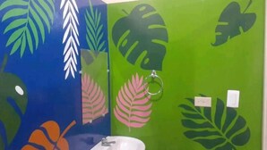A bathroom with a sink and a mirror, walls painted in green and blue with leaf patterns. - Hostel Coco's  (Moyogalpa)