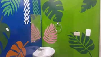 Un baño con lavamanos y espejo, paredes pintadas en verde y azul con motivos de hojas.