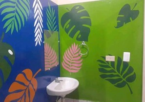Un baño con lavamanos y espejo, paredes pintadas en verde y azul con motivos de hojas.