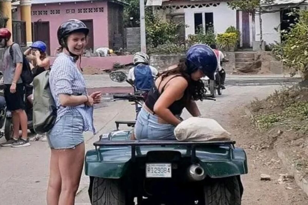 Un grupo de personas de pie en una calle, con un vehículo verde al frente.