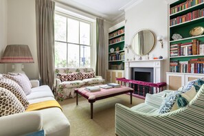 Ein helles Wohnzimmer mit Kamin, einem großen Fenster und einer Bücherwand.