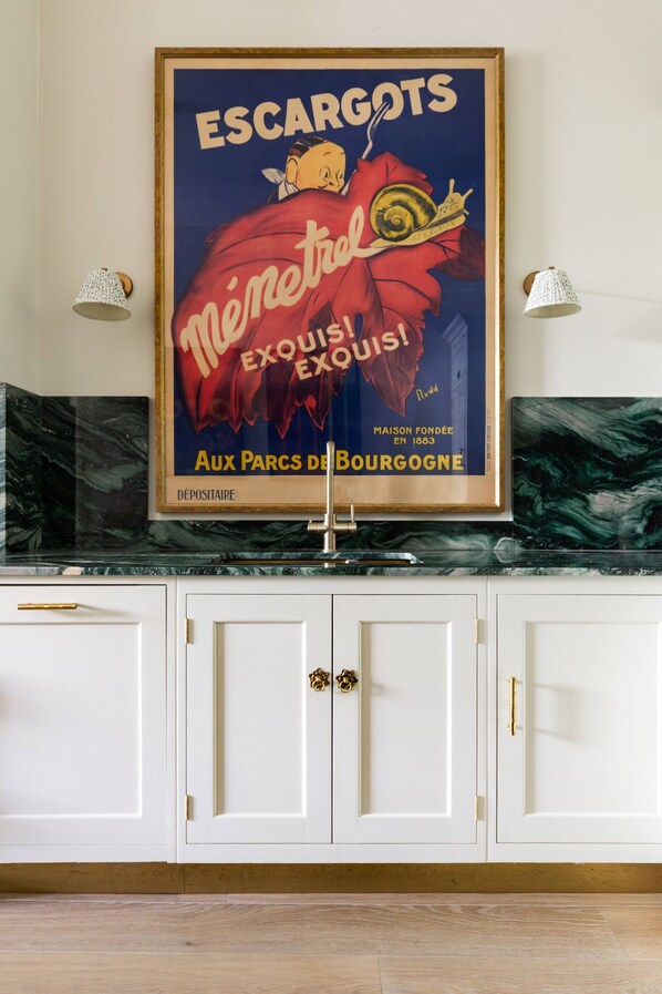 Ein gerahmter, alter Reiseplakat auf einer Küchenarbeitsplatte mit weißen Schränken und einer Marmor-Spritzschutzwand.