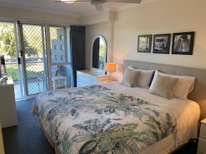 A hotel room with a bed, a desk, a chair, and a view through a glass door. - Belvedere Apartments (Sunshine Coast)