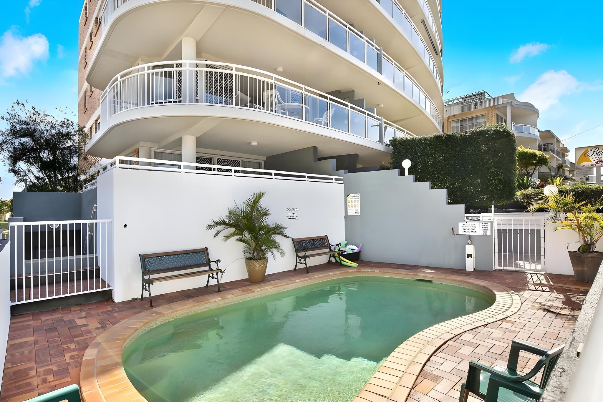 A multi-level residential building with a swimming pool, outdoor seating, and a gated entrance.