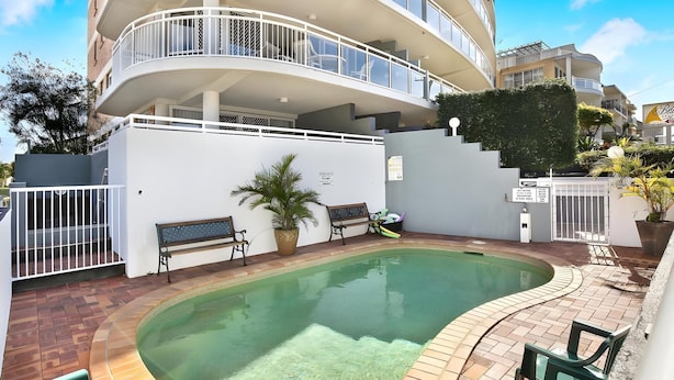 Un edificio residencial de varios niveles con piscina, zona de estar al aire libre y acceso mediante portón cerrado.