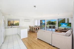 A modern living space with a kitchen, dining area, and a large window with a view of the beach. - Belvedere Apartments (Sunshine Coast)
