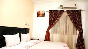 Een hotelkamer met een bed, nachtkastje, telefoon, airconditioning en een raam met gordijnen.