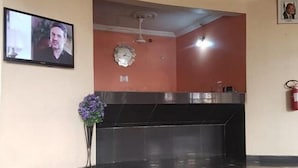 Een receptiegedeelte met een flatscreen televisie, een klok, een vaas met paarse bloemen en een brandblusser.