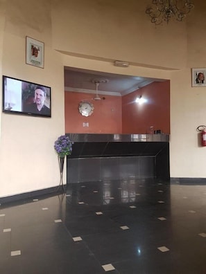 A reception area with a flat-screen TV, a clock, a vase with purple flowers, and a fire extinguisher. - Clen Phil Hotels And Suites (Port Harcourt)