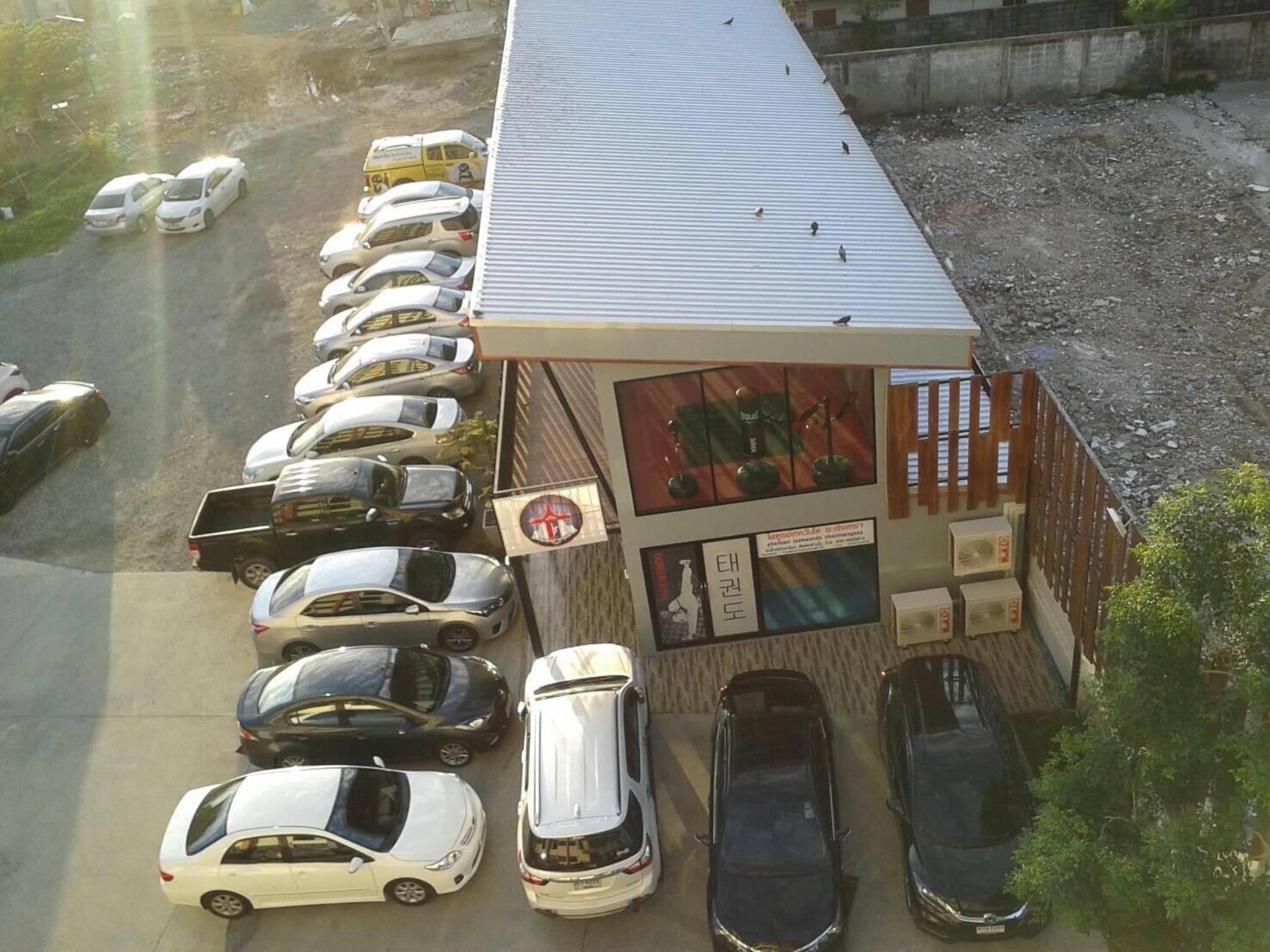 A parking lot with multiple cars parked in rows, a building with a sloped roof, and a sign with Korean text.