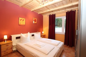 Quarto com duas camas, teto de madeira, janela com cortinas e obras de arte na parede.