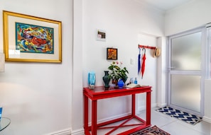 A hallway with a red console table, a framed abstract painting, and a door with frosted glass panels. - Bleu Cobalt Cottage (Franschhoek)