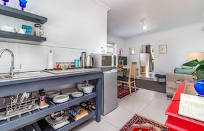 A modern kitchen with a built-in microwave, kettle, and coffee maker. There is a dining area with a wooden chair and a red table. - Bleu Cobalt Cottage (Franschhoek)