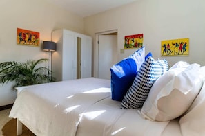 Quarto com cama, almofadas, guarda-roupa e obras de arte na parede.