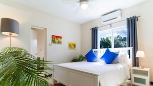 Une chambre à coucher comprenant un lit, une table de chevet, une lampe, un ventilateur de plafond et une fenêtre avec des rideaux.