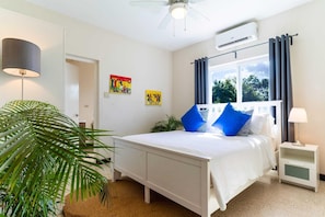 Quarto com cama, mesa de cabeceira, abajur, ventilador de teto e janela com cortinas.