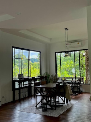 Ein Essbereich mit Tisch und Stühlen, große Fenster mit Blick auf Grünflächen und eine Klimaanlage.