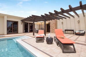 A poolside area with lounge chairs, a pergola, and a stone wall. - Casa Rural La Morisca (Tuineje)