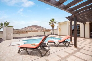 A poolside area with two sun loungers, a pergola, and a view of a mountain. - Casa Rural La Morisca (Tuineje)
