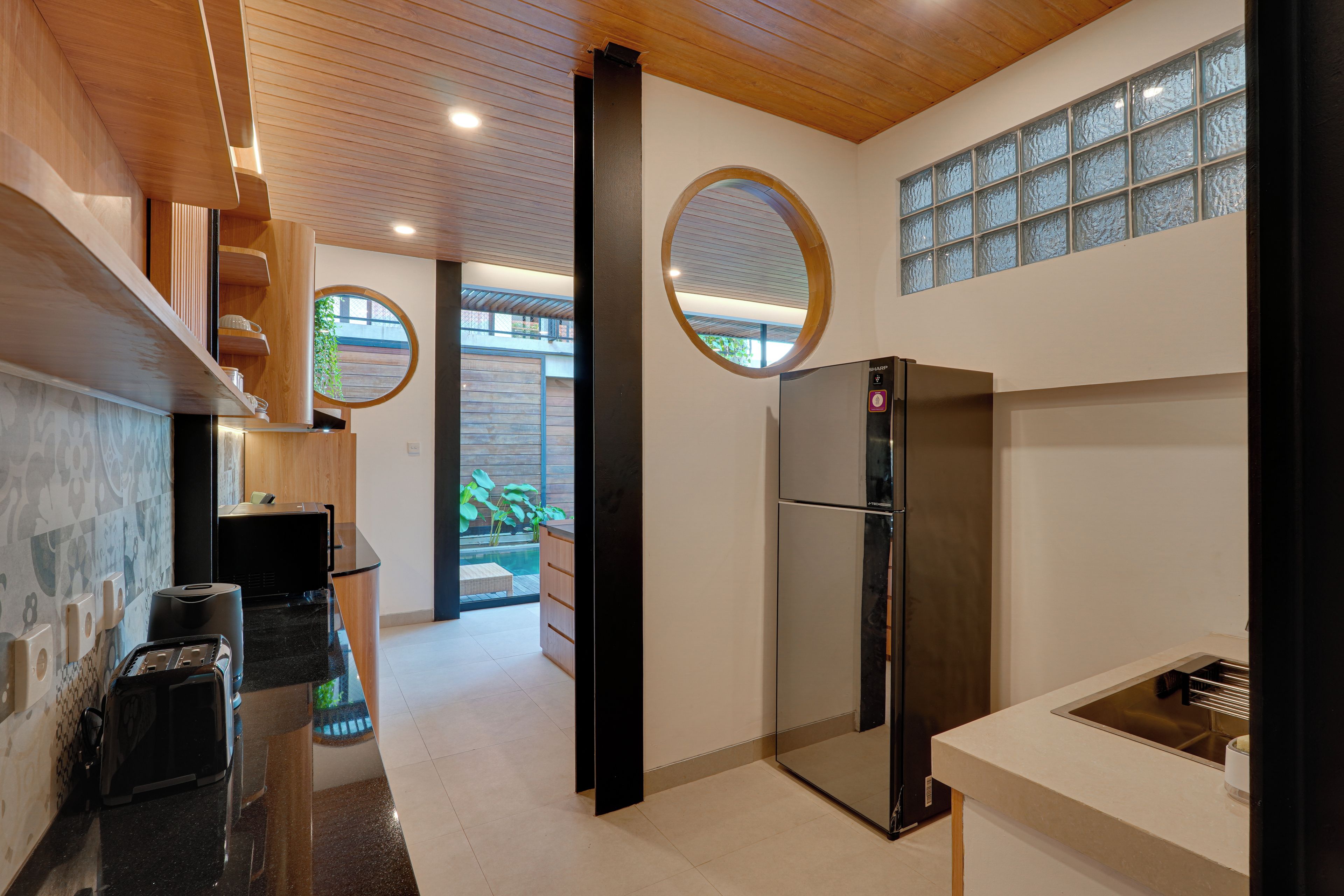 A modern kitchen with a stainless steel refrigerator, wooden cabinets, and a large window with a view of the outdoors.