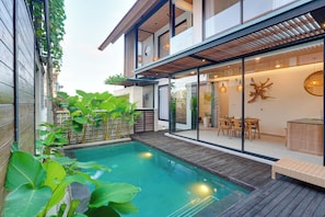 Ein modernes Haus mit Swimmingpool, Holzterrasse und Essbereich mit Tisch und Stühlen.