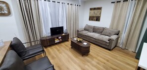 A living room with a sofa, a coffee table, a TV on a stand, and a painting on the wall. - 4bedroom home in amazing Atlanta conveniently located no matter what your plans. (Atlanta)