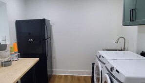 A compact kitchen with a black refrigerator, a washing machine, a sink, and a wooden table with various items. - 4bedroom home in amazing Atlanta conveniently located no matter what your plans. (Atlanta)