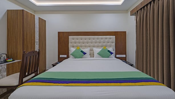 Quarto de hotel com uma cama grande, guarda-roupa de madeira, secretária com cadeira e janela com cortinas.