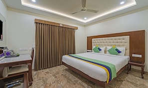 A hotel room with a bed, a desk, a chair, a ceiling fan, and a window with curtains. - Treebo Trend Aaravi Residency (Puducherry)