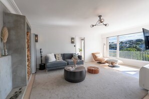 A modern living room with a grey sofa, a round coffee table, and a large window with a view of a residential area. - Hidden Treasure 3 bedrooms in the Prime Location (Auckland City)
