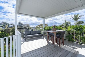 A covered outdoor area with a wooden deck, a sofa, and a table with chairs. - Hidden Treasure 3 bedrooms in the Prime Location (Auckland City)