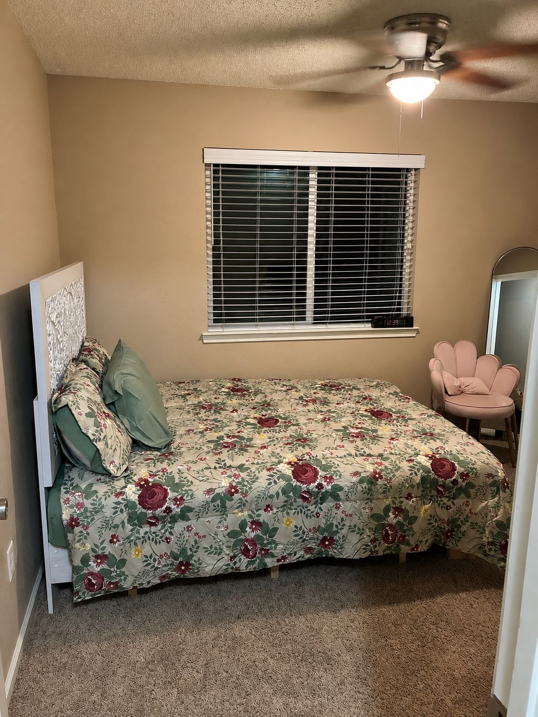 A bedroom with a bed, a window with blinds, a ceiling fan, and a chair.
