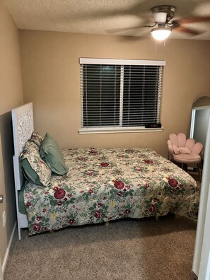Un dormitorio con cama, ventana con persianas, ventilador de techo y una silla.