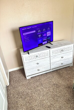 A flat-screen TV on a white dresser with intricate carvings, displaying a streaming service interface. - Entire Katy cozy home (Katy)