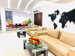 Eine moderne Hotellobby mit einer Sofagarnitur, einem Couchtisch mit Blumenarrangement und einer Weltkarte an der Wand.