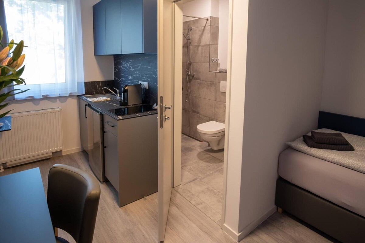 Habitación de hotel compacta con kitchenette, ducha y cama.