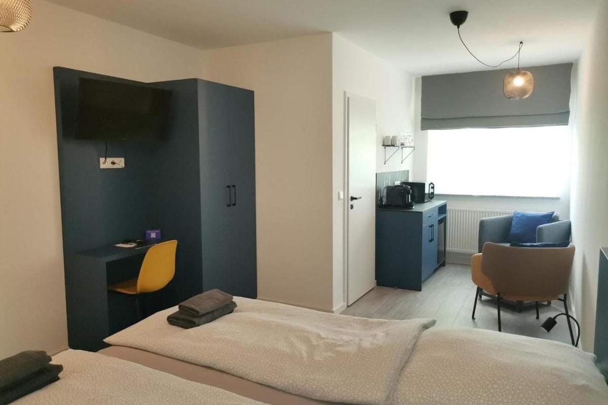 Habitación de hotel con cama, escritorio, silla, kitchenette y vistas al exterior.