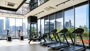 Gimnasio con cintas de correr, bicicletas estáticas y un espejo, con vistas a la ciudad a través de amplias ventanas.