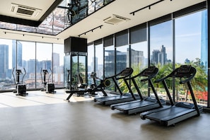 Ein Fitnessstudio mit Laufbändern, Fahrrädern und einer Spiegelwand, mit Blick auf die Stadt durch große Fenster.