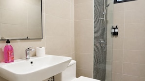 Un baño con lavamanos blanco, inodoro y cabina de ducha con paredes de vidrio.